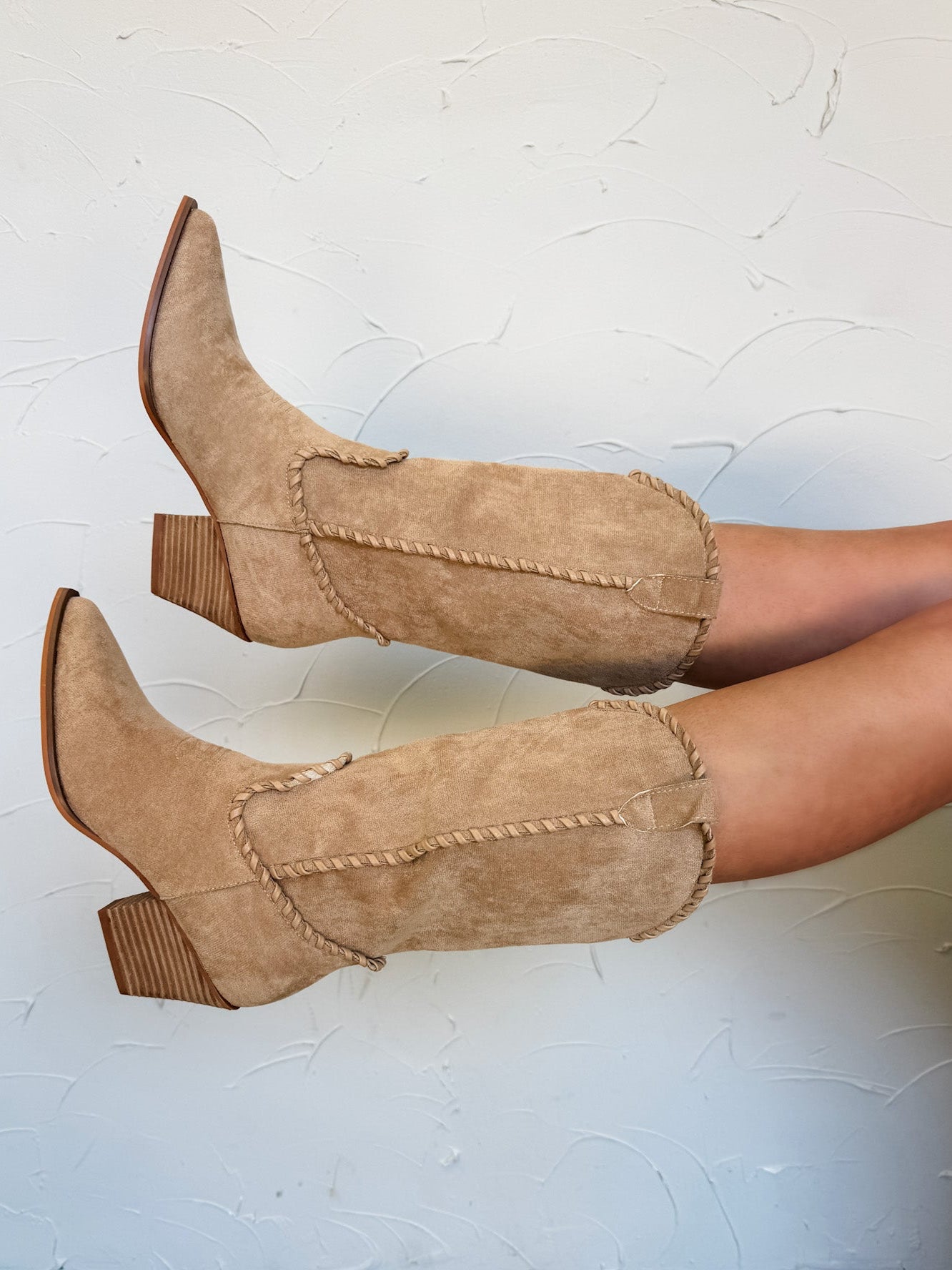 Tan suede boots with decorative stitching on a white background