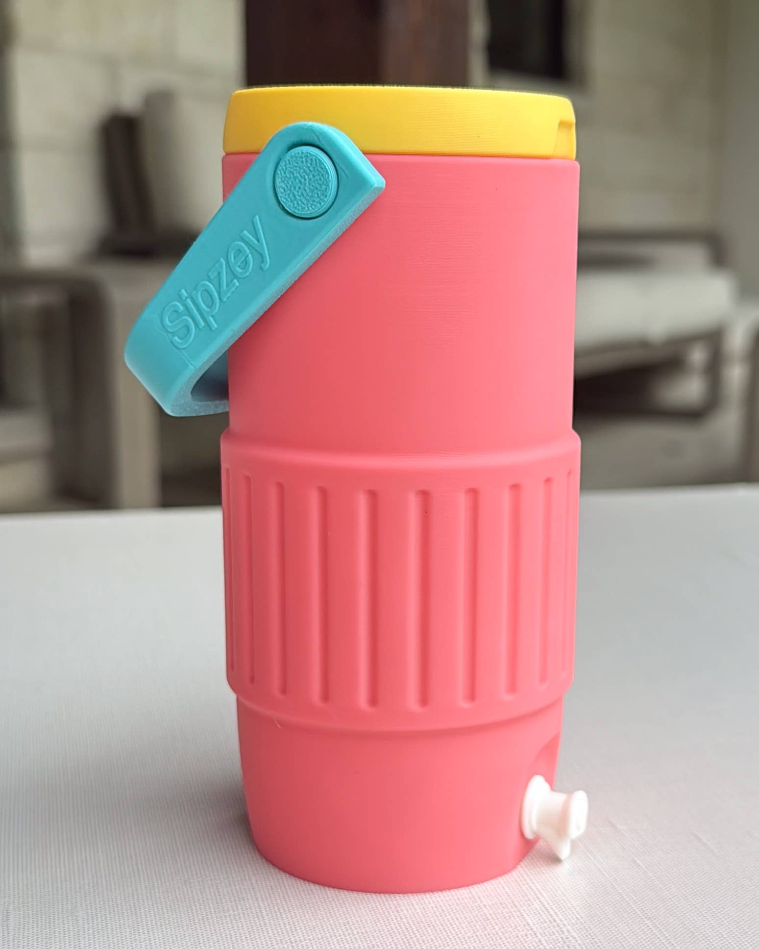 Pink silicone water bottle with a yellow cap and blue opener on a white surface.