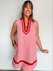 Woman wearing a red and white checkered dress against a white wall.