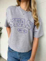 Person wearing a gray t-shirt with 'SFASU' printed on it against a white wall.