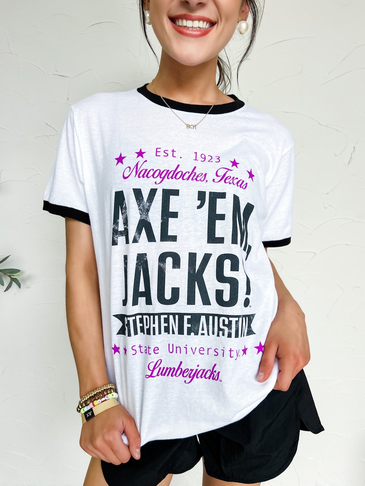 Person wearing a white baseball style t-shirt with SFA text and black shorts on a plain background