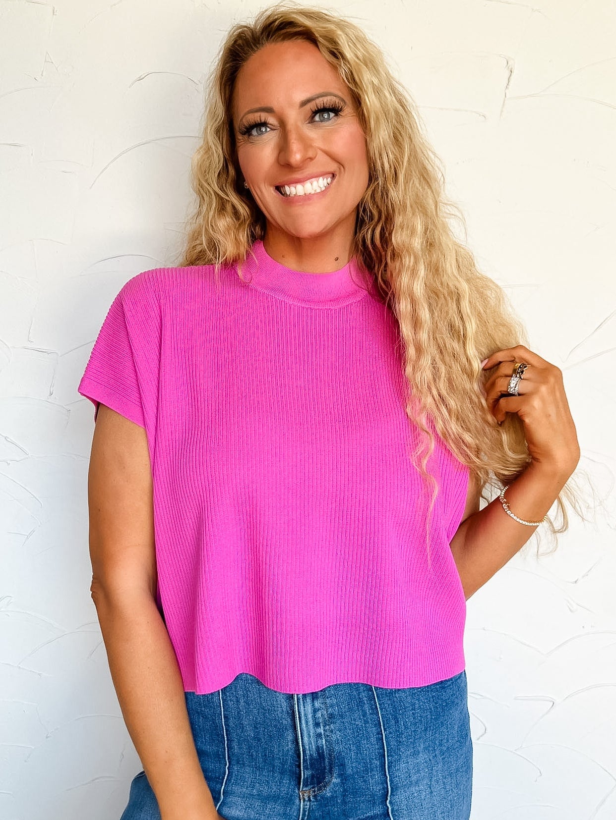 Woman wearing a bright pink sleeveless top and blue jeans against a white background
