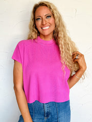 Woman wearing a bright pink sleeveless top and blue jeans against a white background