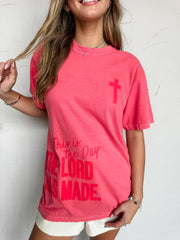 Person wearing a pink t-shirt with a cross and text against a white background