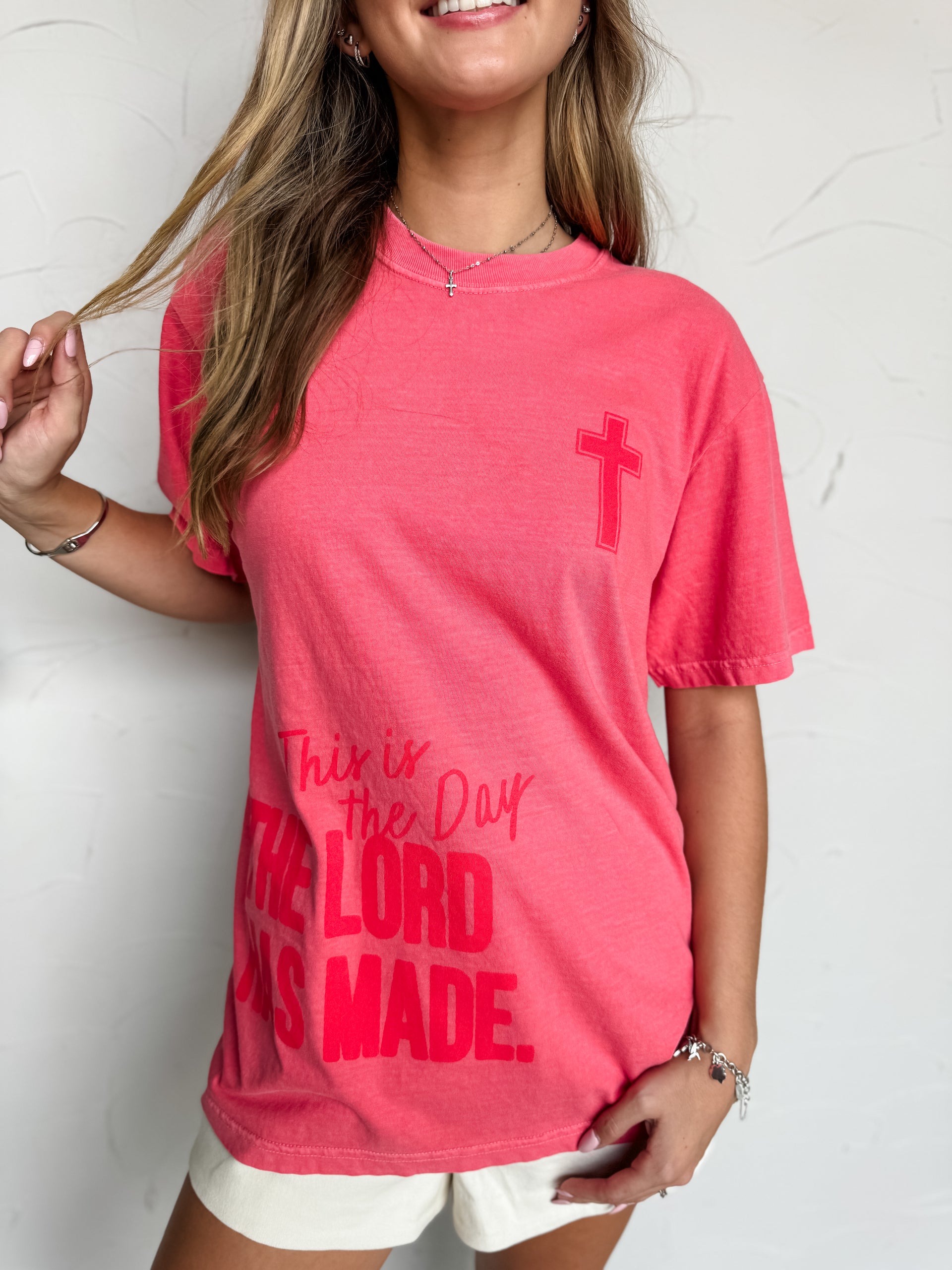 Person wearing a pink t-shirt with a cross and text against a white background
