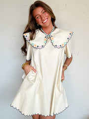 Woman wearing a white dress with a colorful embroidered collar against a white background