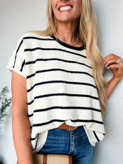 Woman wearing a black and white striped shirt with blue jeans against a light background