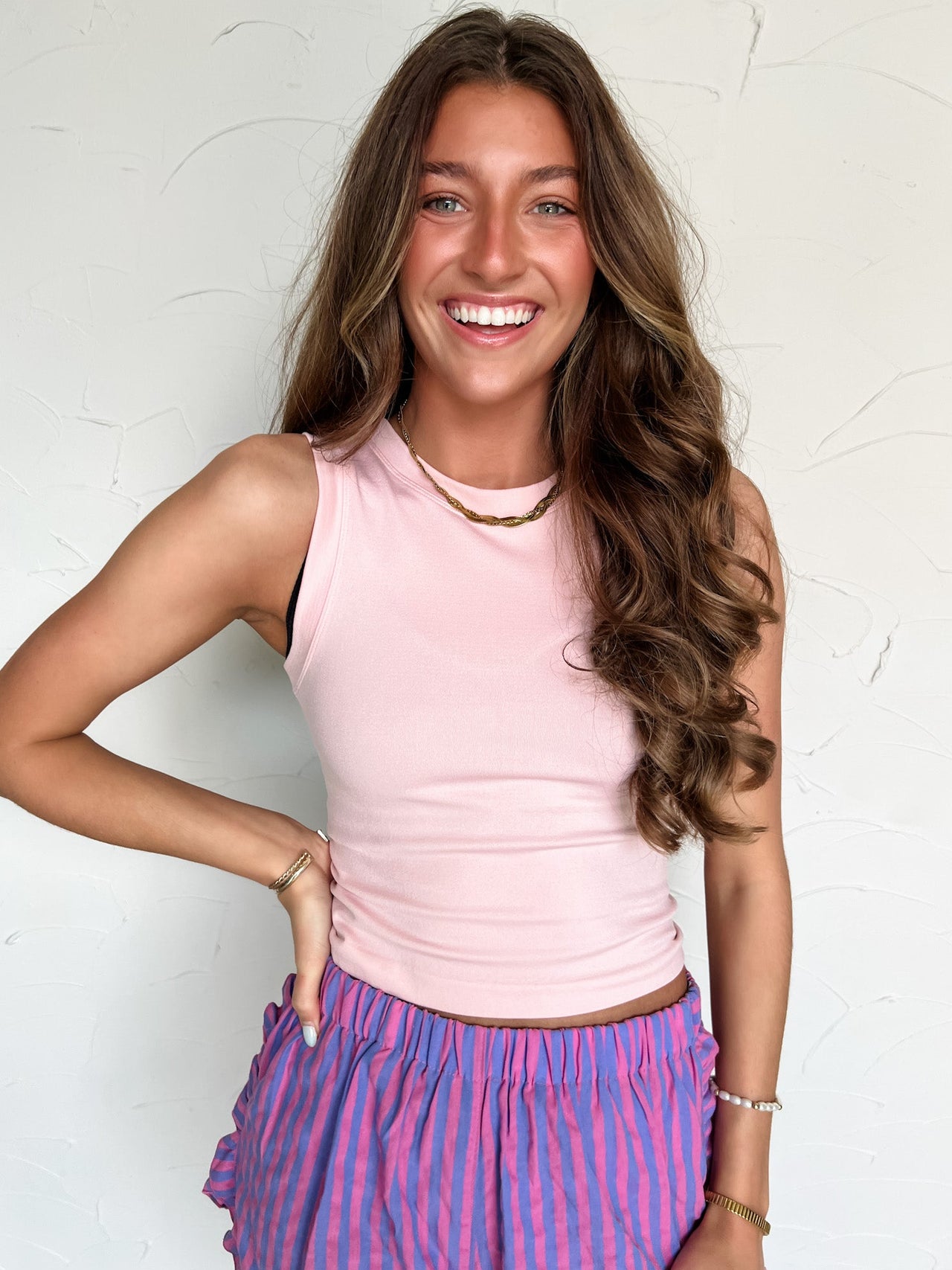 Woman wearing a pink sleeveless top and purple striped pants against a white background