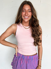 Woman wearing a pink sleeveless top and purple striped pants against a white background