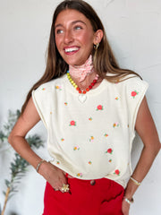 Woman wearing a cream blouse with floral embroidery and red pants against a white background