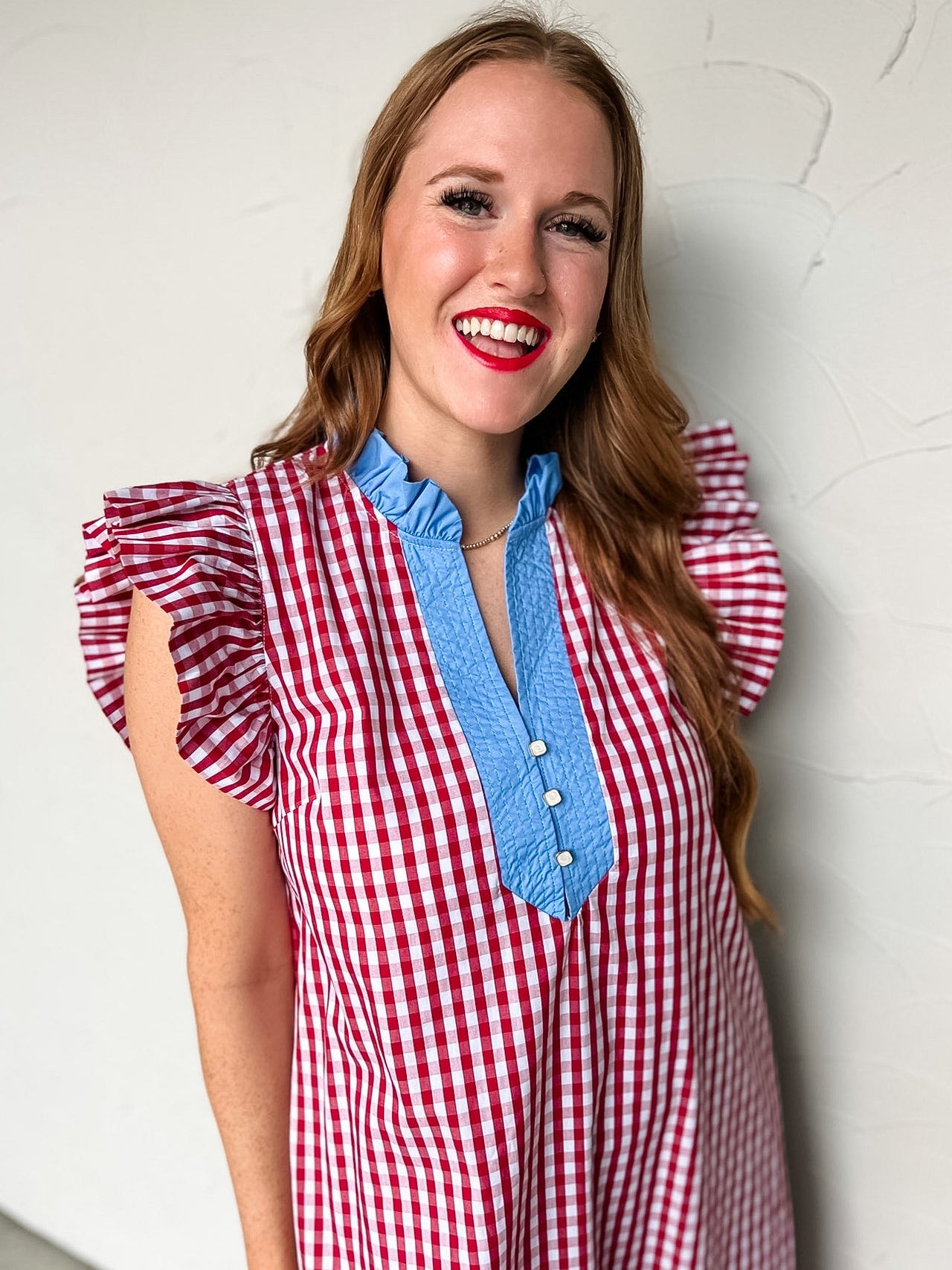 Woman wearing a red and white checkered dress with blue trim against a light gray wall.