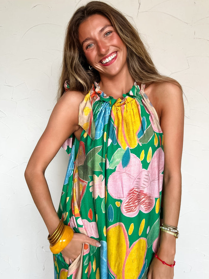 Woman wearing a long colorful floral halter neck dress against a white background