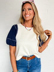 Woman wearing a white and navy baseball  style shirt with blue jeans against a white background