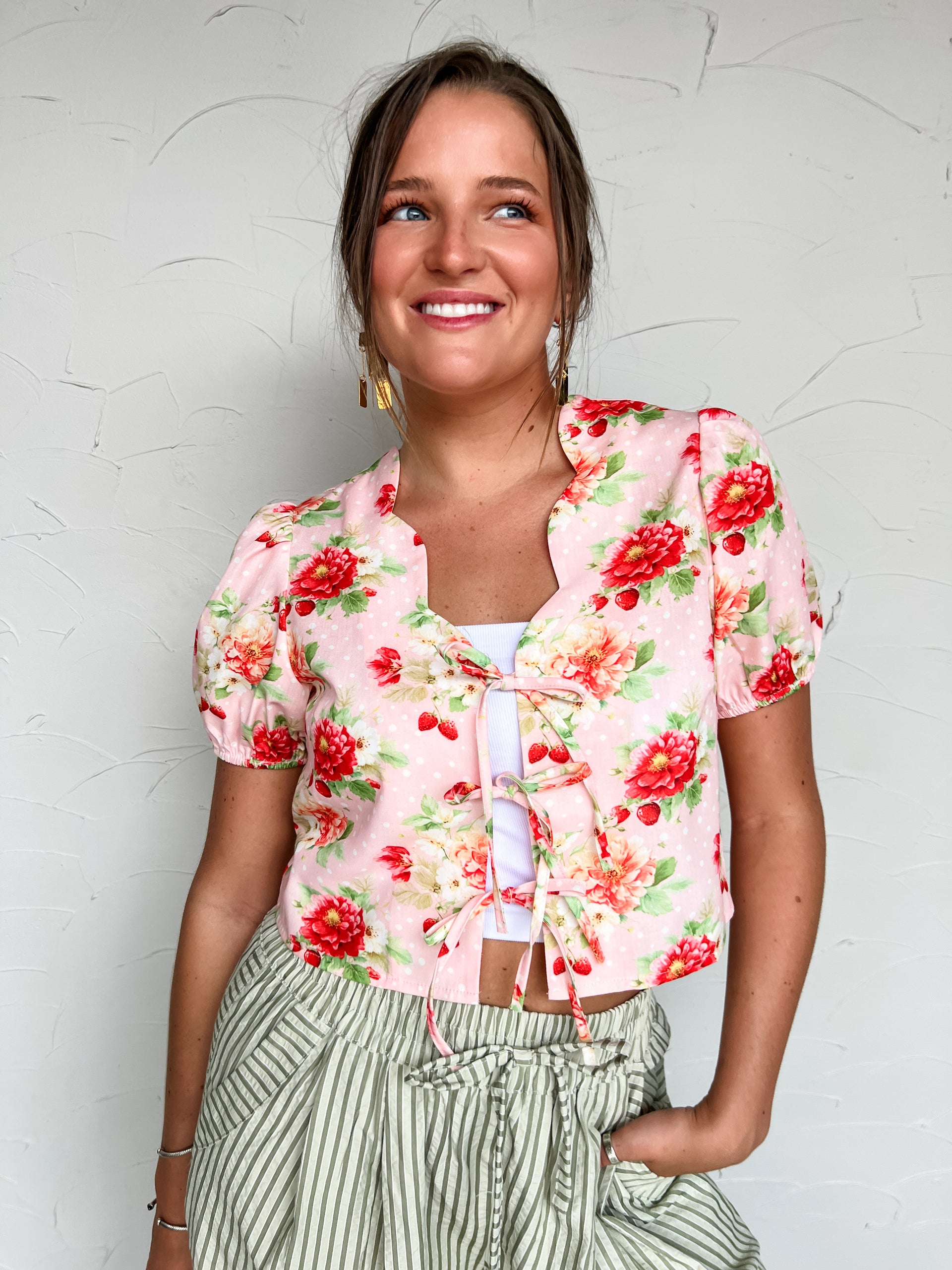 Woman wearing a floral pink top with red flowers against a light gray background
