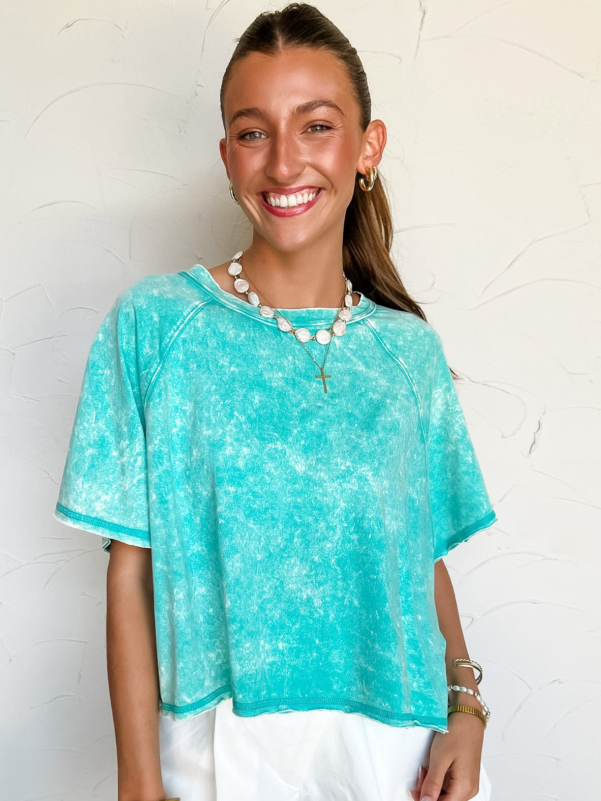 Woman wearing a turquoise cropped top and white shorts against a light background