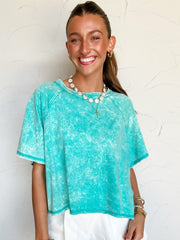 Woman wearing a turquoise cropped top and white shorts against a light background