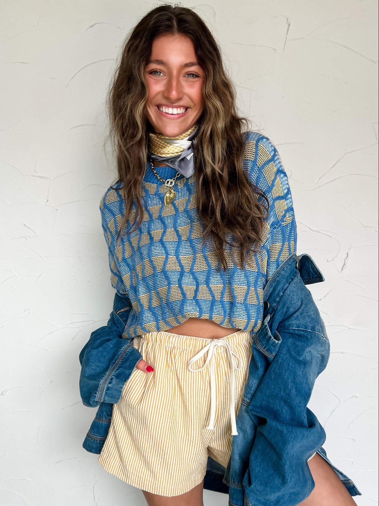 Woman wearing a blue patterned sweater and beige shorts against a white wall