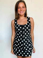 Woman wearing a black dress/romper with white polka dots against a white background