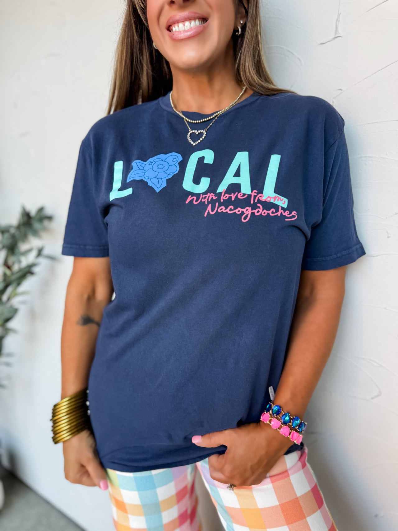 Woman wearing a navy blue t-shirt with colorful text and graphics, standing against a white wall.