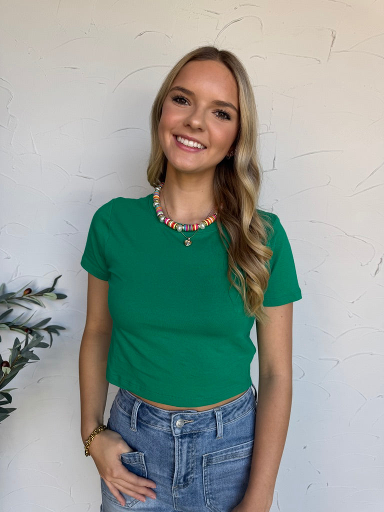 Woman wearing a green t-shirt and blue jeans against a white textured wall.
