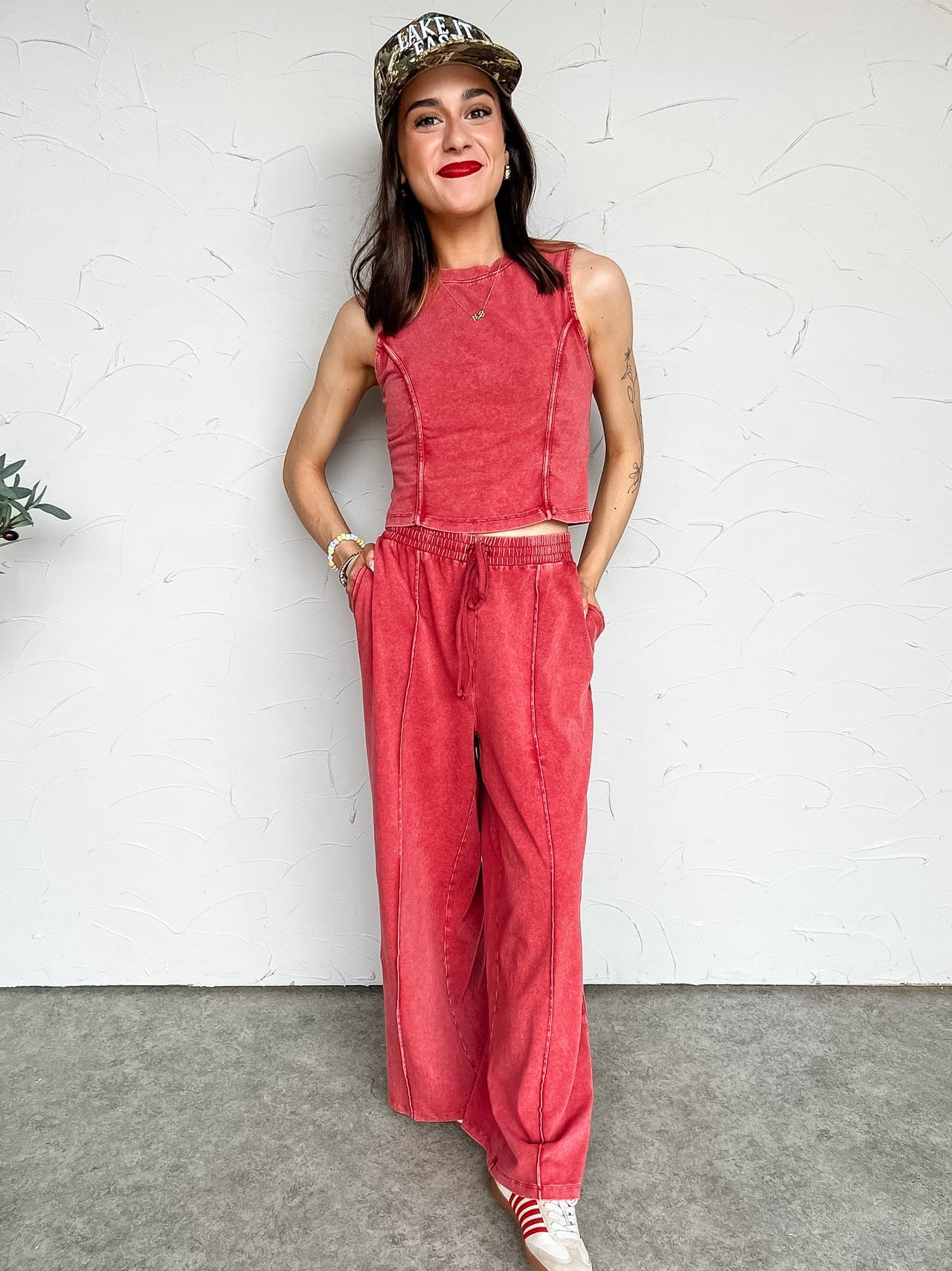 Woman wearing a red acid washed  set and cap against a white wall