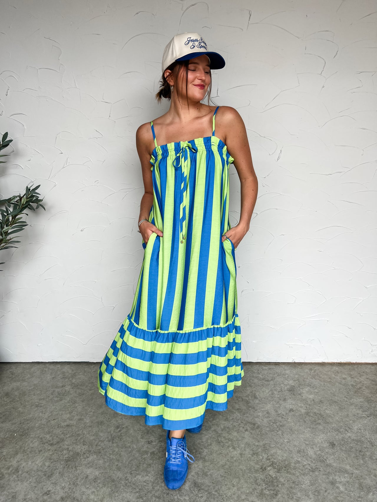 Person wearing a blue and green striped dress with a white cap against a white wall.