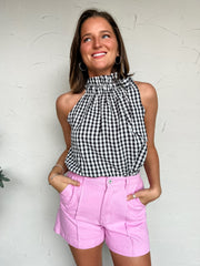 Woman wearing a black and white Gingham top and pink shorts against a white wall.