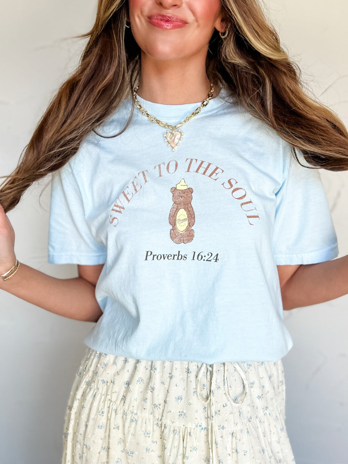 Woman wearing a light blue t-shirt with text and graphics, standing against a plain background.