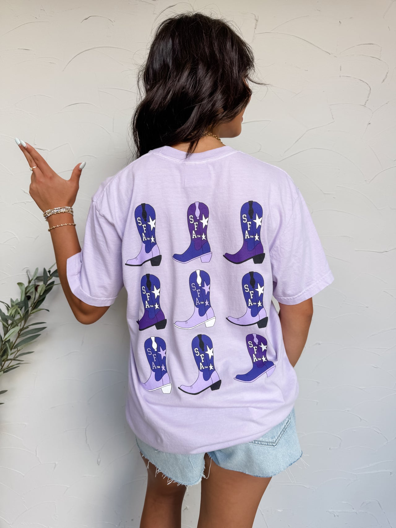 Person wearing a light purple t-shirt with blue cowboy boot designs on the back, standing against a white wall.