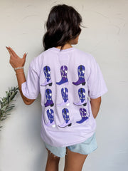 Person wearing a light purple t-shirt with blue cowboy boot designs on the back, standing against a white wall.