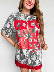Woman wearing a camo graphic tee with red text "free indeed, john 8:36" against a white background
