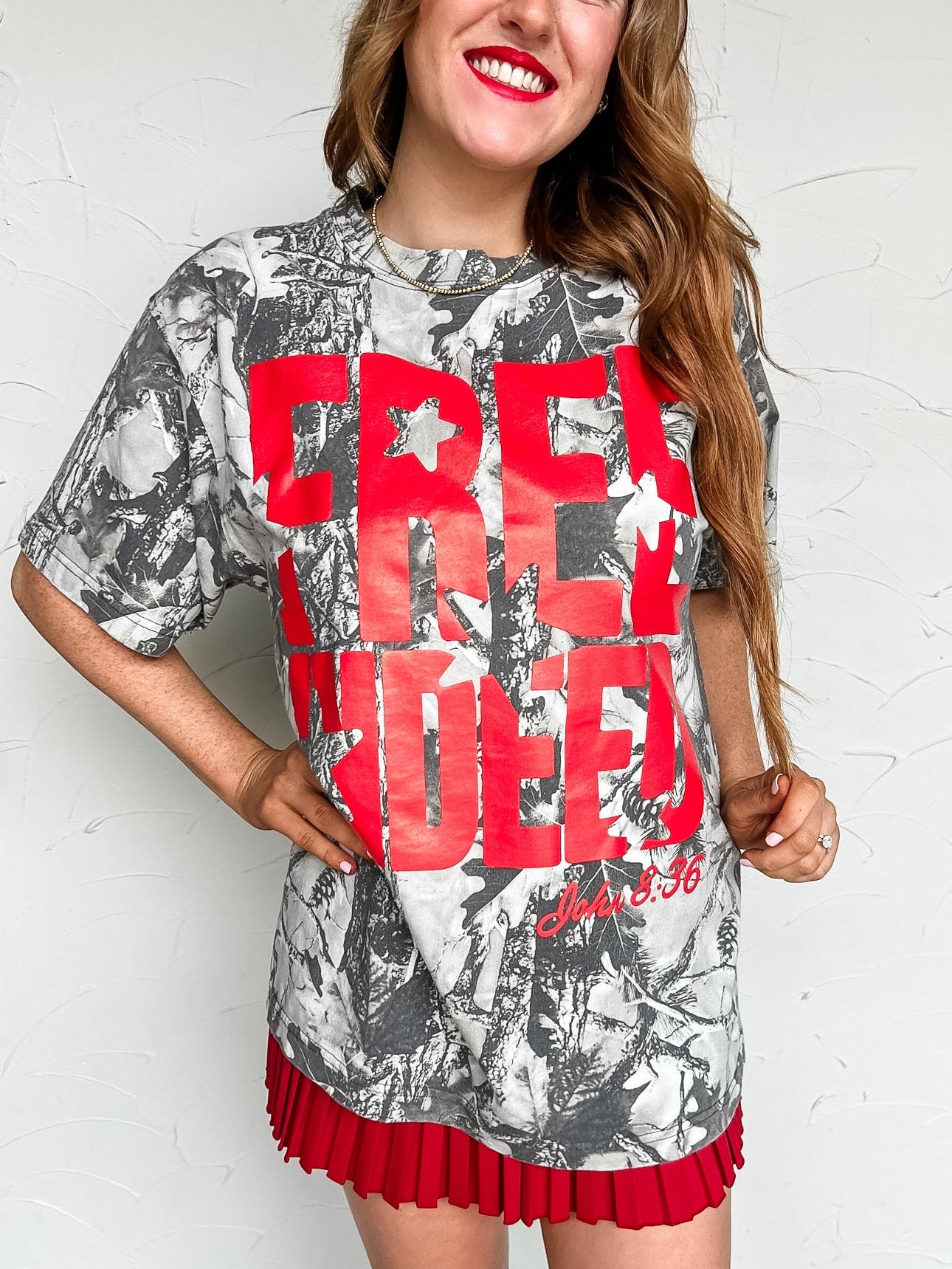 Woman wearing a camo graphic tee with red text "free indeed, john 8:36" against a white background