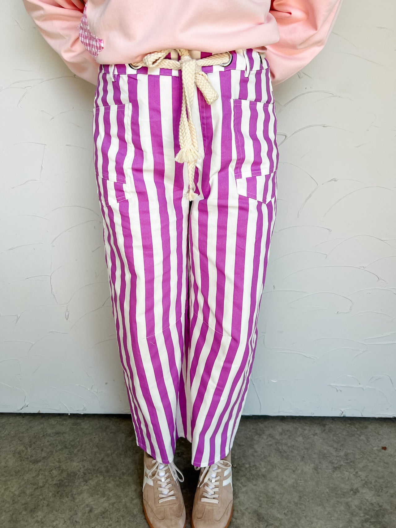 Person wearing pink sweatshirt and purple and white striped pants against a white wall.