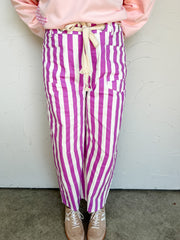 Person wearing pink sweatshirt and purple and white striped pants against a white wall.