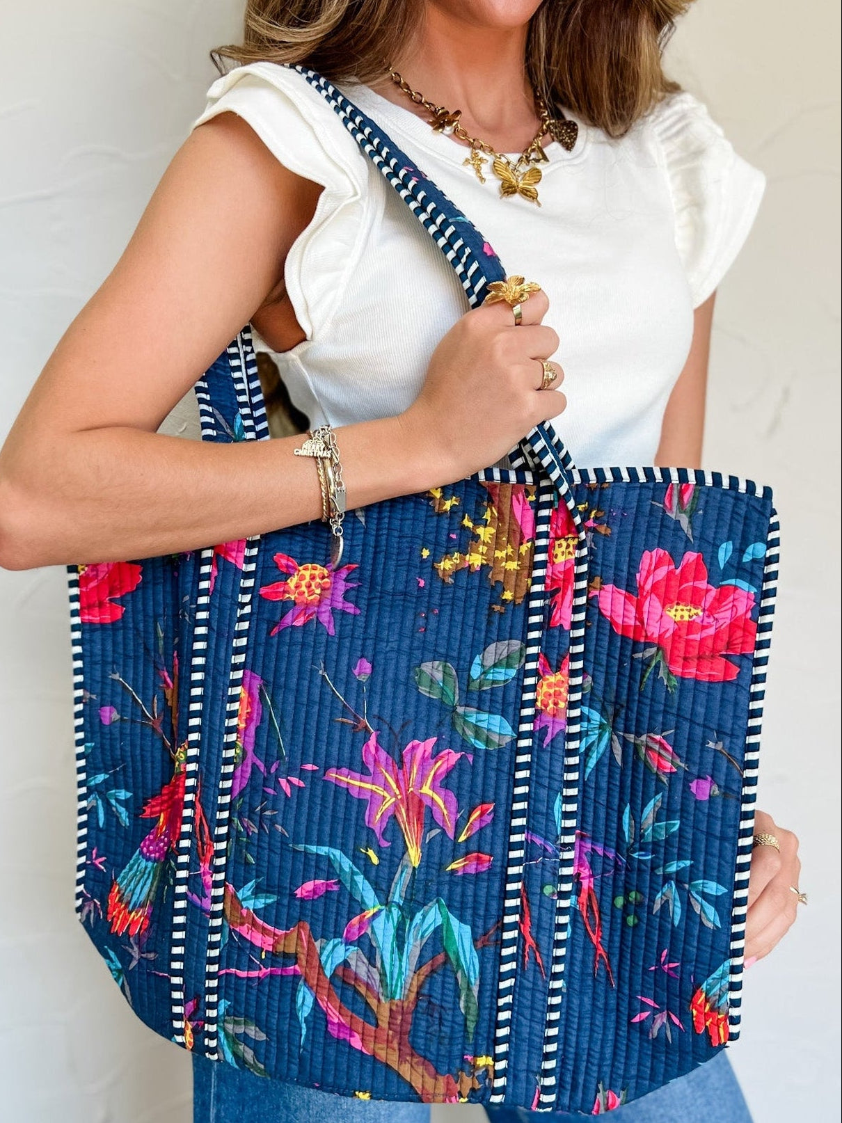 Person holding a navy blue bag with colorful bird pattern and striped handle.