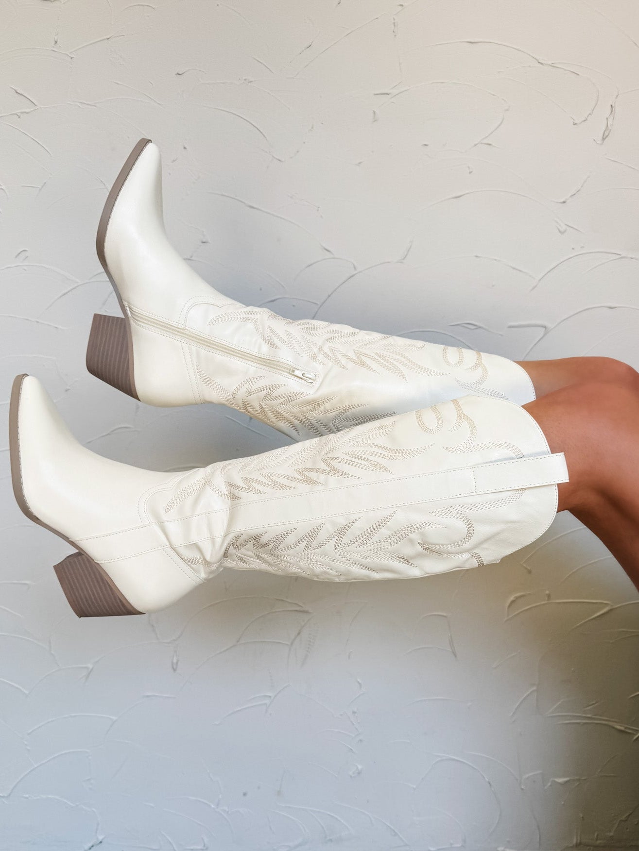 White cowboy boots being worn against a white wall.