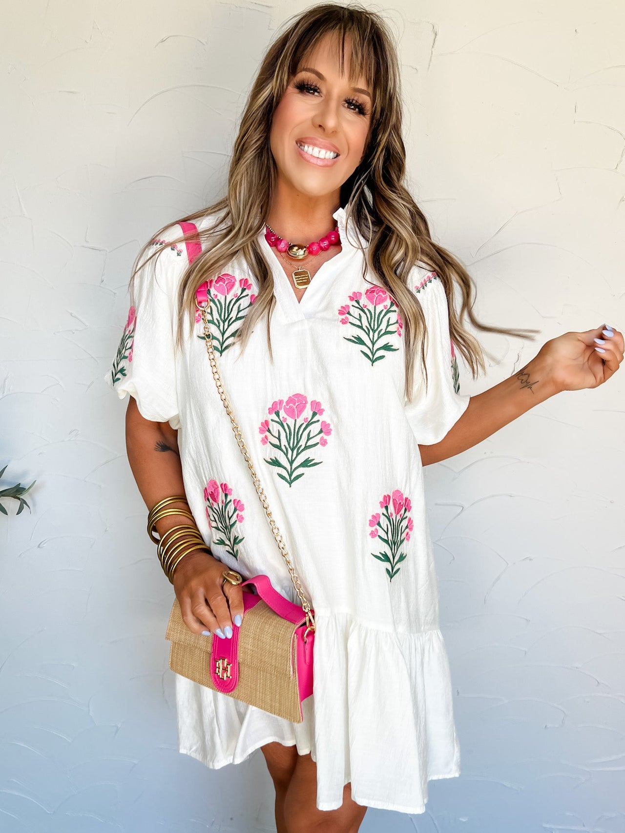 Woman wearing a white dress with floral embroidery against a white wall.