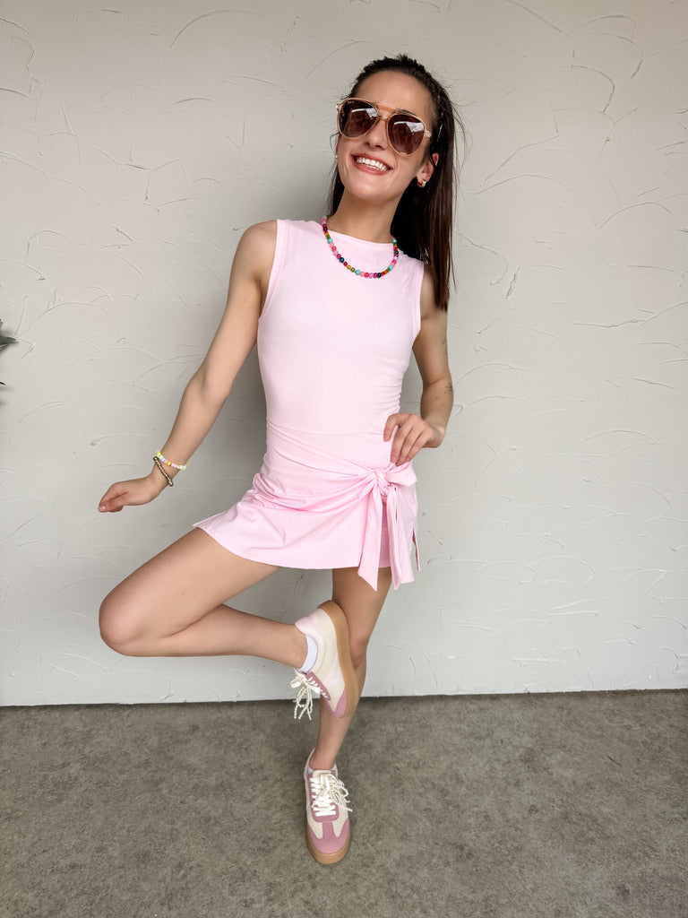 Woman in a pink dress posing against a plain wall.