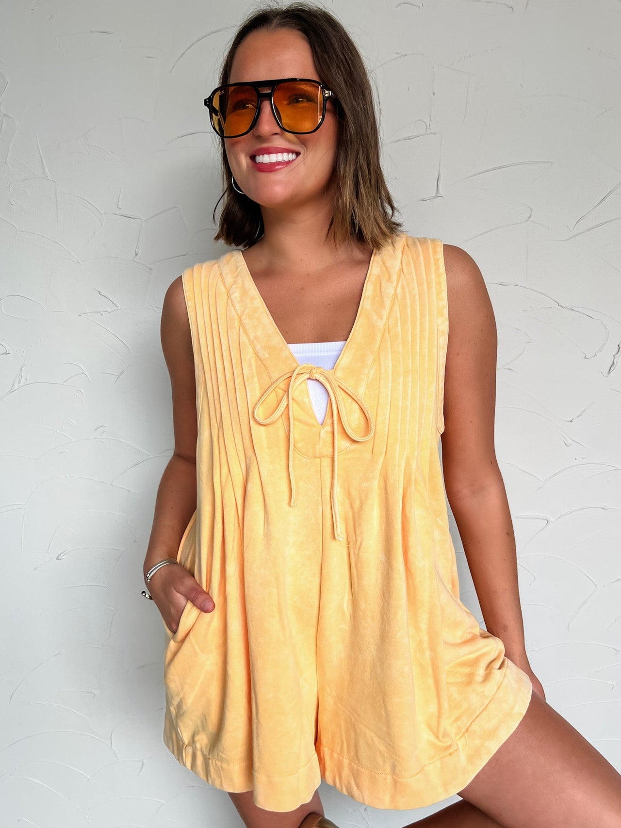 Woman wearing an orange romper with sunglasses against a white background
