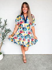 Woman wearing a colorful floral dress against a white wall.