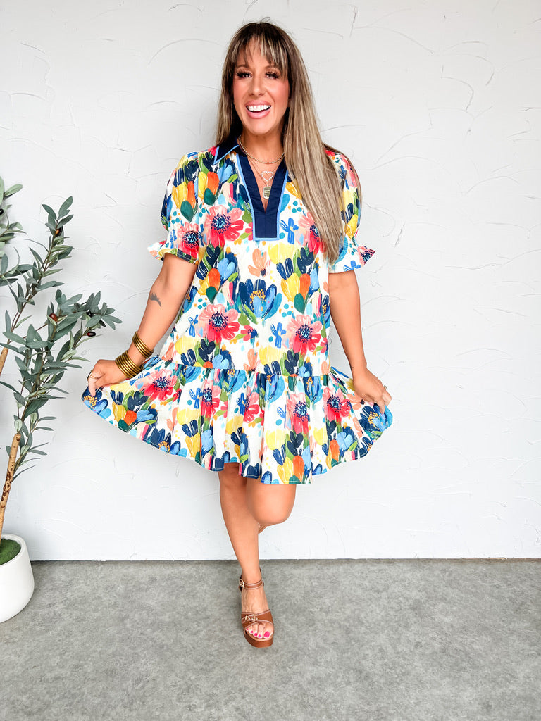 Woman wearing a colorful floral dress against a white wall.