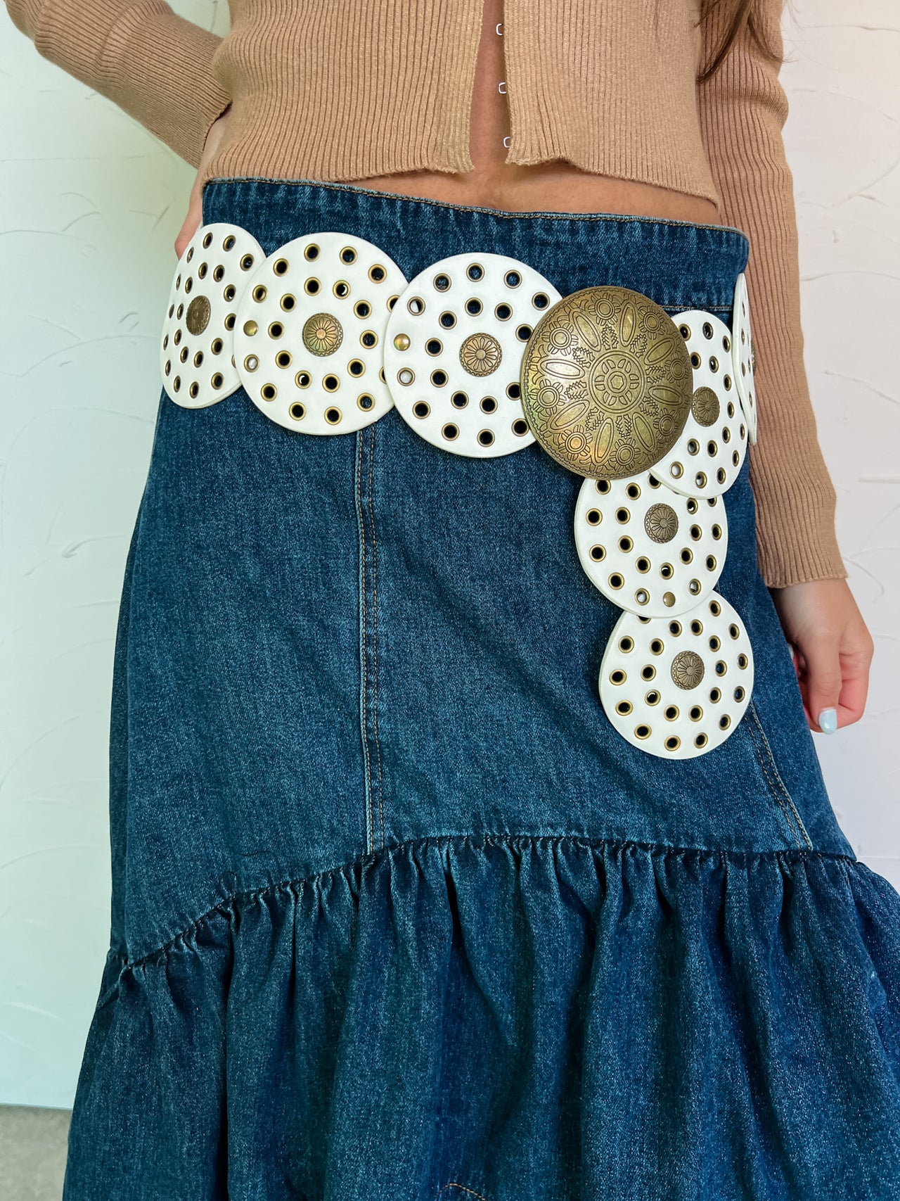 Model wearing a Western-inspired belt with faux-leather discs and an antique gold center over a denim skirt.