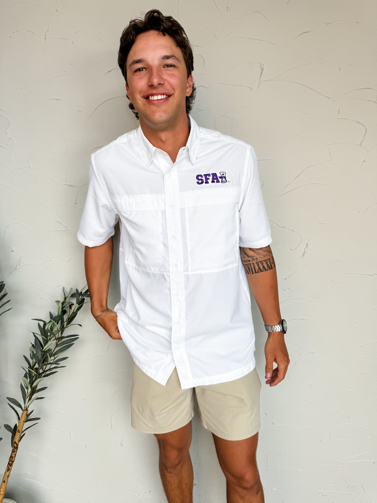 Man wearing a white button-up shirt with a logo, standing against a plain background