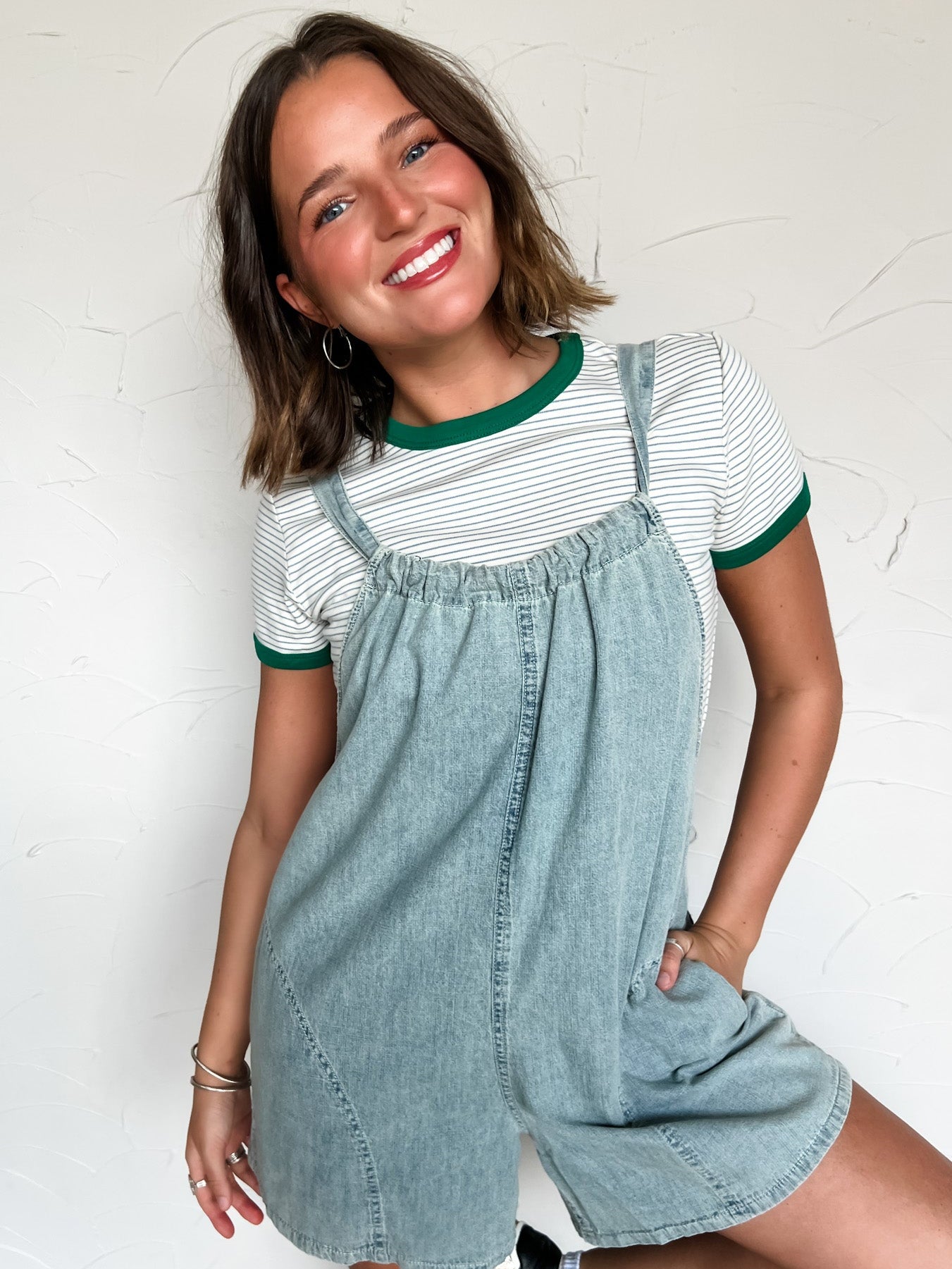 Woman wearing a striped shirt and denim overalls against a white wall