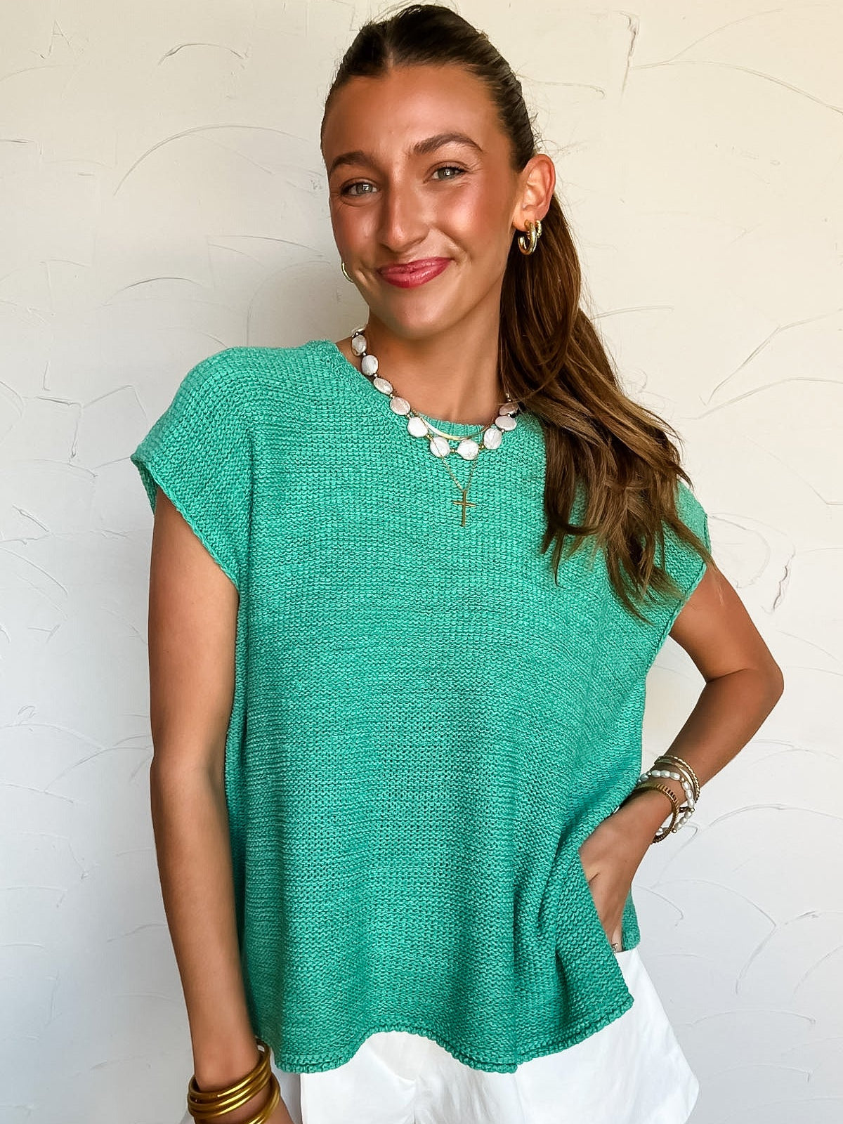 Woman wearing a green knit top and white shorts against a light background