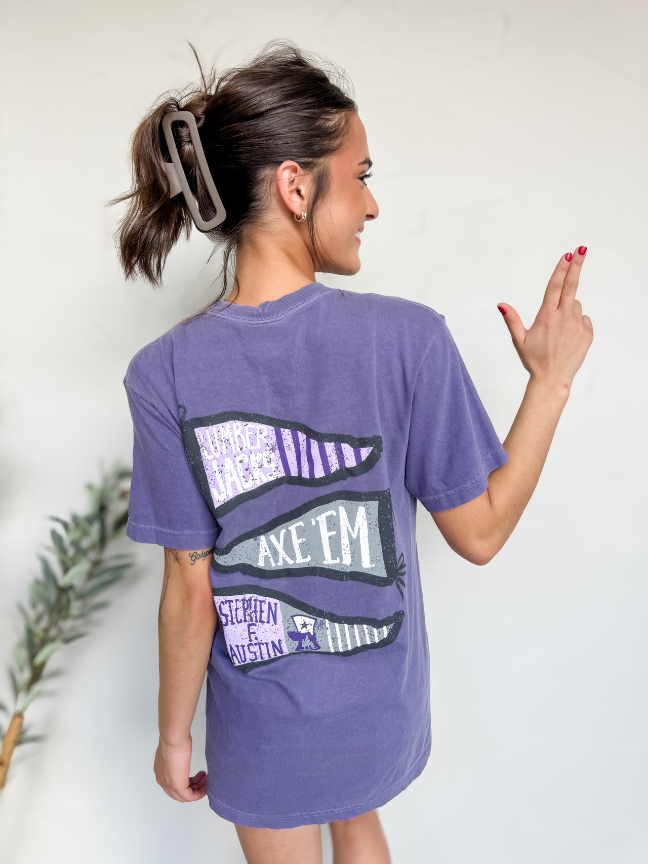 Woman wearing a purple t-shirt with a graphic design on the back, standing against a plain background.