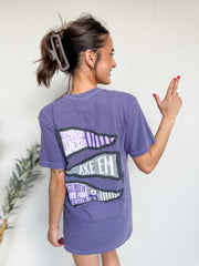 Woman wearing a purple t-shirt with a graphic design on the back, standing against a plain background.