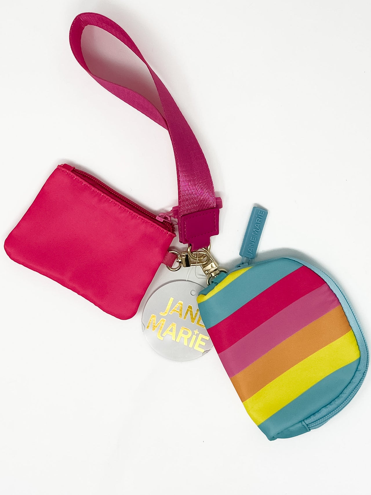 Pink wristlet with two zipper pouches, one with multi color striped against a white wall.