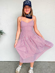 Woman wearing a red and white striped midi dress with a blue cap against a white wall.