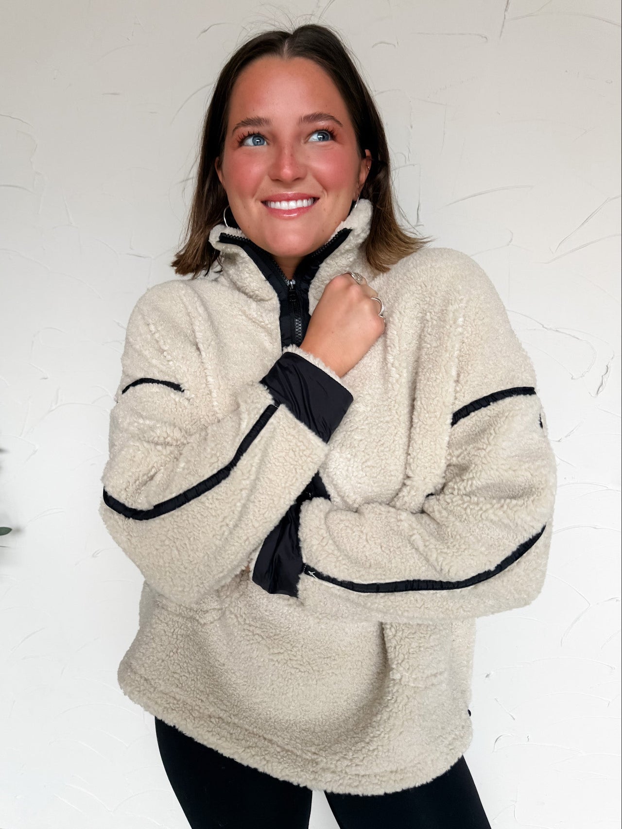 Woman wearing a beige fleece jacket with black detail against a white background